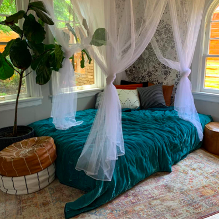 Reviewer image with mattress in the corner of the room. The simple bed looks really put together with floor pillows on either end, fancy bedding, and the canopy hanging from the ceiling. 