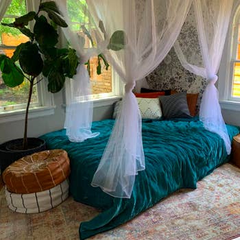 Reviewer image with mattress in the corner of the room. The simple bed looks really put together with floor pillows on either end, fancy bedding, and the canopy hanging from the ceiling. 