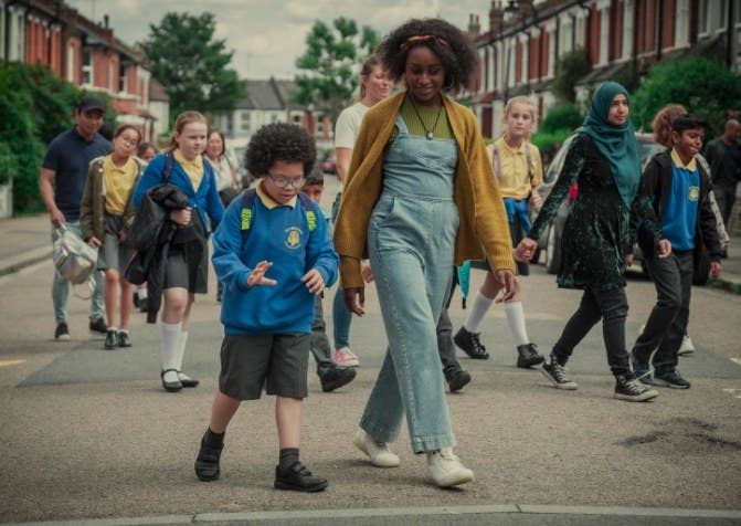Louise walks next to Adam in his school uniform in a crowd of school kids and their parents