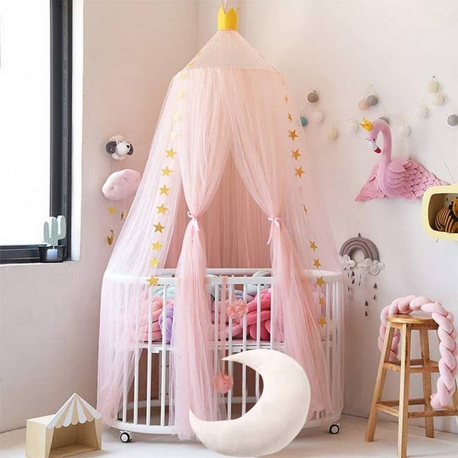 Canopy draped over small crib hanging from the ceiling to the floor. It has a small crown on top. 