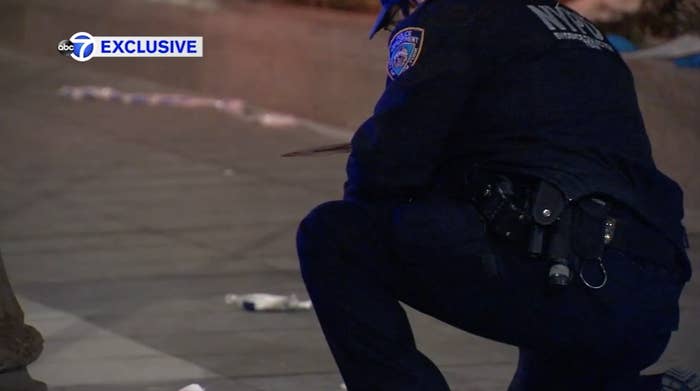A NYPD officer kneels on the sidewalk after picking up a bloody knife