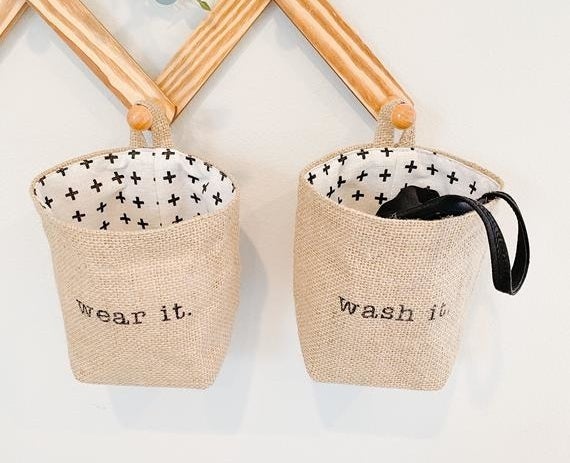 Two baskets hanging from pegs on the wall with one that says &quot;wear it&quot; and &quot;wash it&quot; 