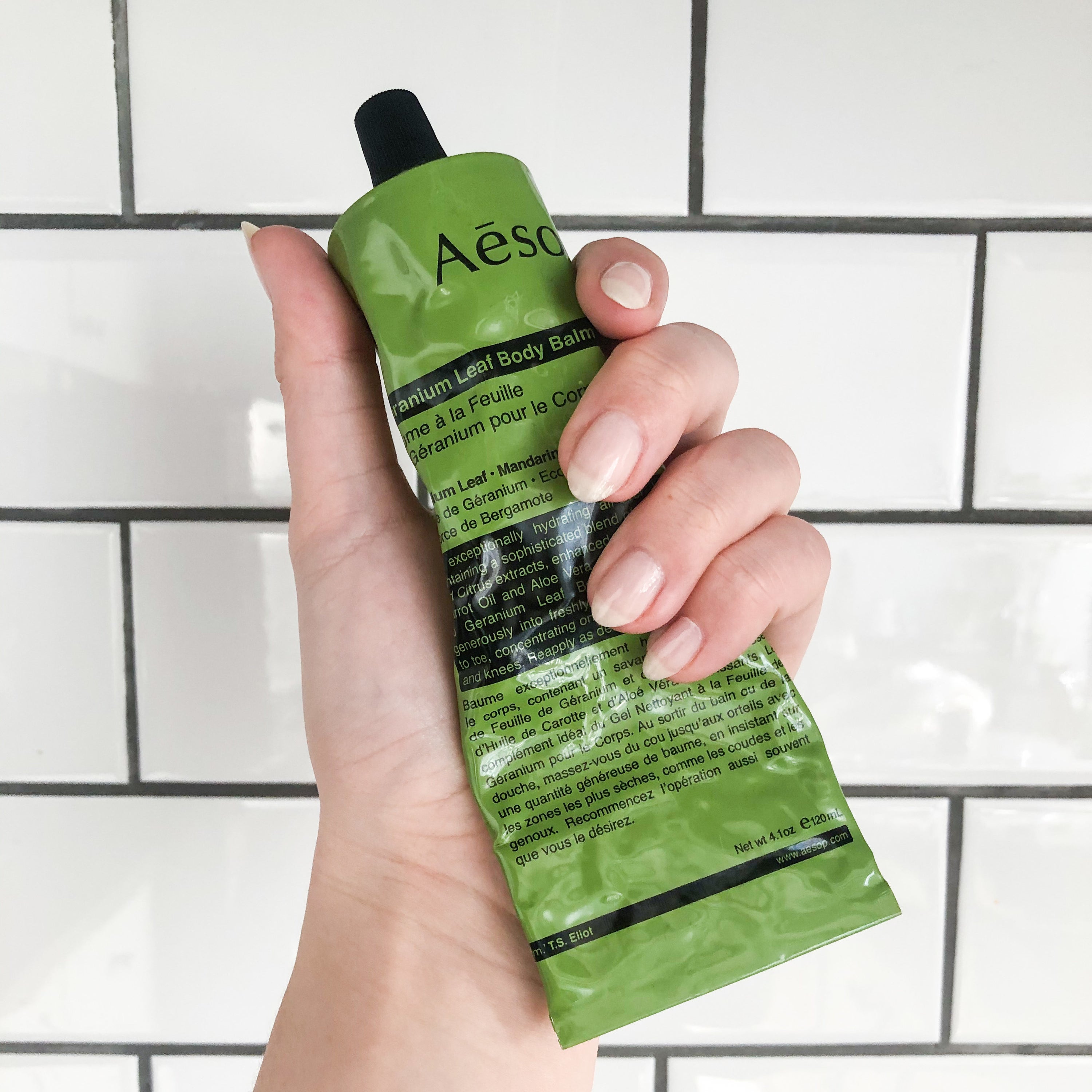 A hand holds a tube of the body balm