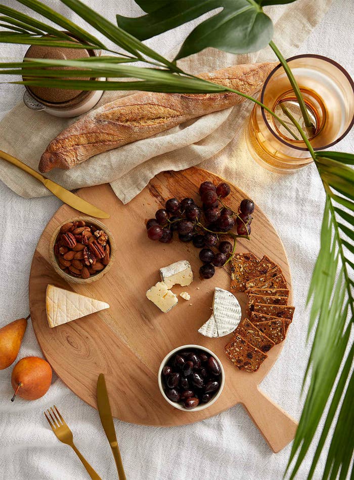 A round wooden tray with cheese, crackers, and grapes on it