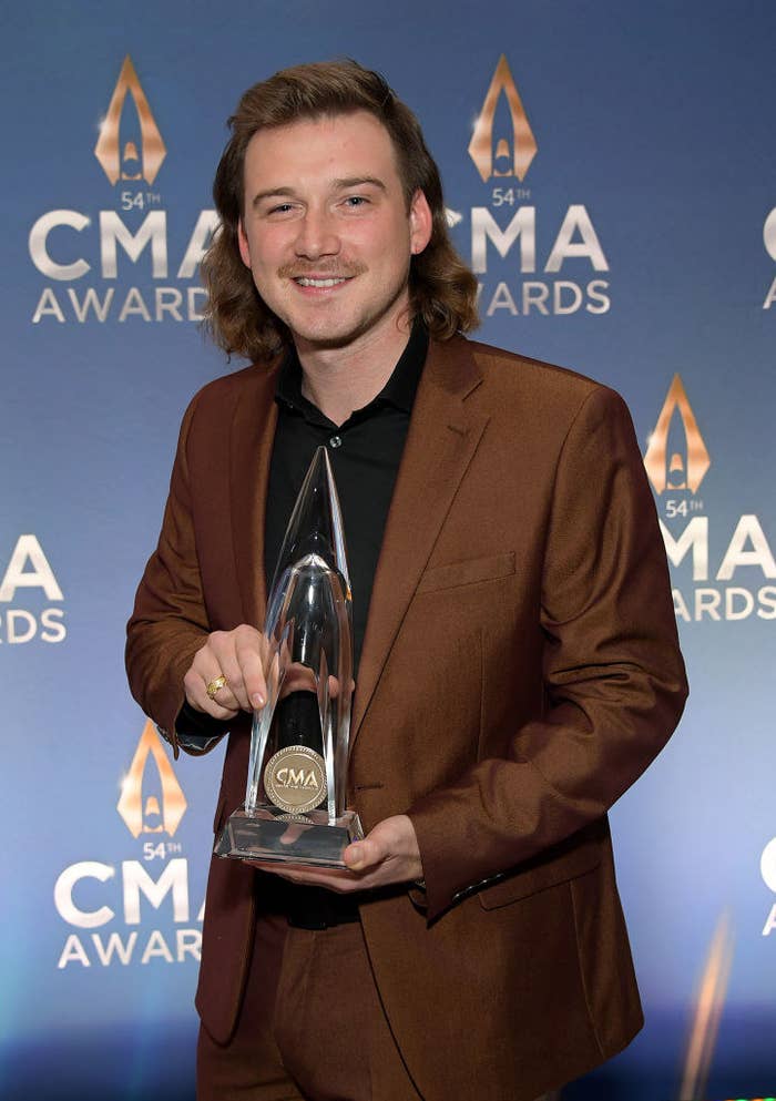 Morgan, in a suit, posing with his Country Music Award