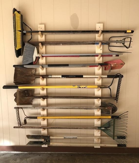 A wall-mounted organizer with pegs to horizontally store yard tools like rakes and shovels 