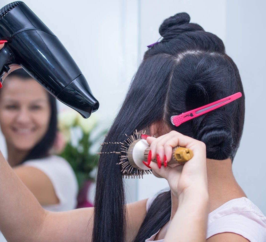 A person blowdrying their hair with a clip holding an already styled piece in place