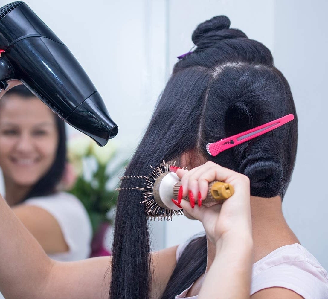 A person blowdrying their hair with a clip holding an already styled piece in place