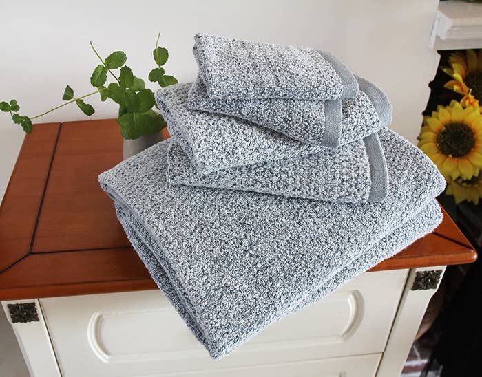 a folded set of grey blue everplush diamond jacquard towels on a wooden cabinet