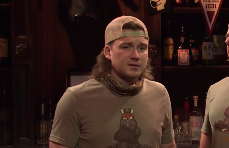 Morgan wearing a baseball cap backwards and a camo scarf in a scene from Saturday Night Live