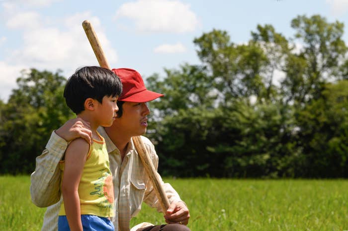 Steven Yeun crouched next to child actor Alan S. Kim in an open field in Minary