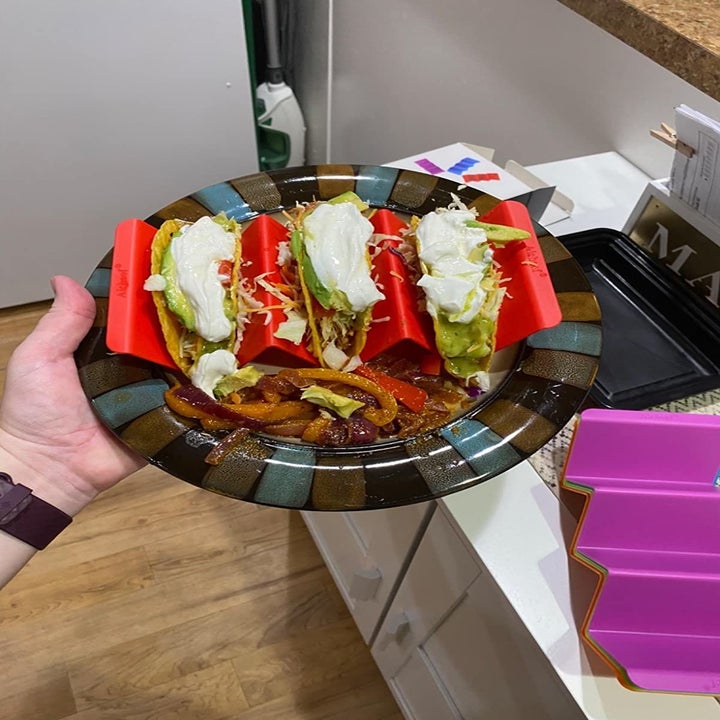 Hand holds plate with red taco holders and shelled tacos inside