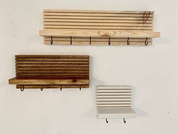 Three wall-mounted wood entryway organizers with multiple key hooks and a shelf in different sizes and colors