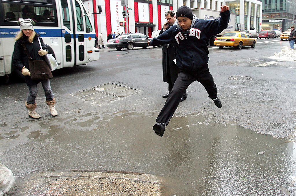 A man wearing a FUBU jacket commits and leaps across a slush pool