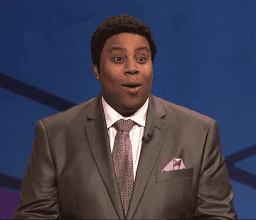 Kenan Thompson, as a game host, looks surprised before furrowing his brows and pursing his lips in thought