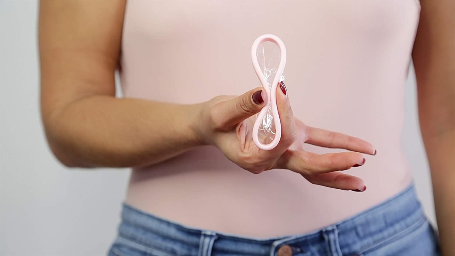 A person holding out the menstrual disc and pinching it between their fingers