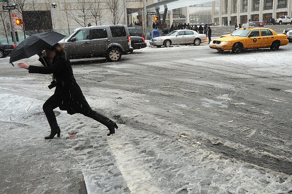 A person carrying an umbrella and walking in boots over a slushy street