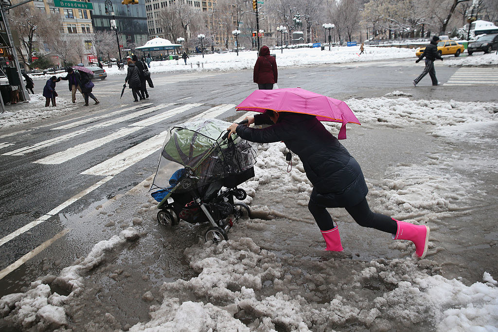 A person trying their best to push a child in a stroller through slush so they can go across a walkway