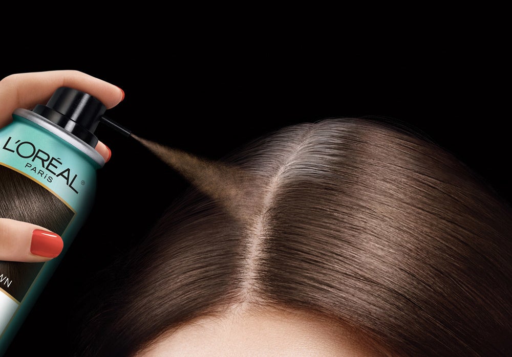 A person applying the concealer spray to their grey roots