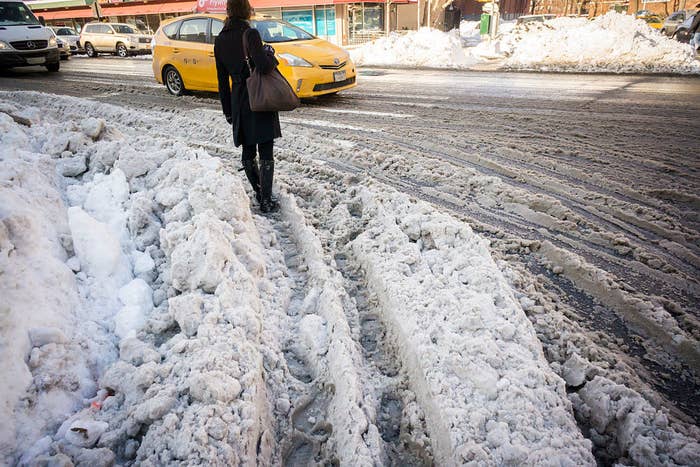 A person standing in plowed snow where a vehicle has driven through as they wait for traffic to stop