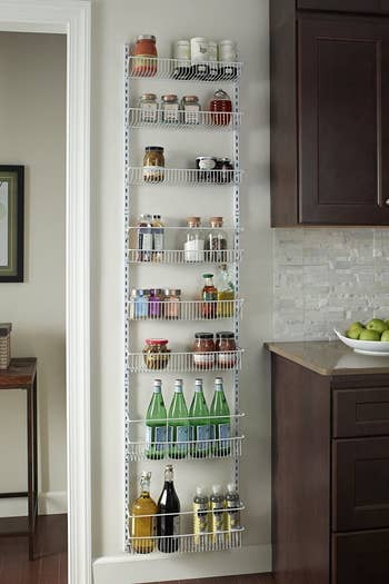 the white tiered rack mounted to the wall and filled with pantry items 
