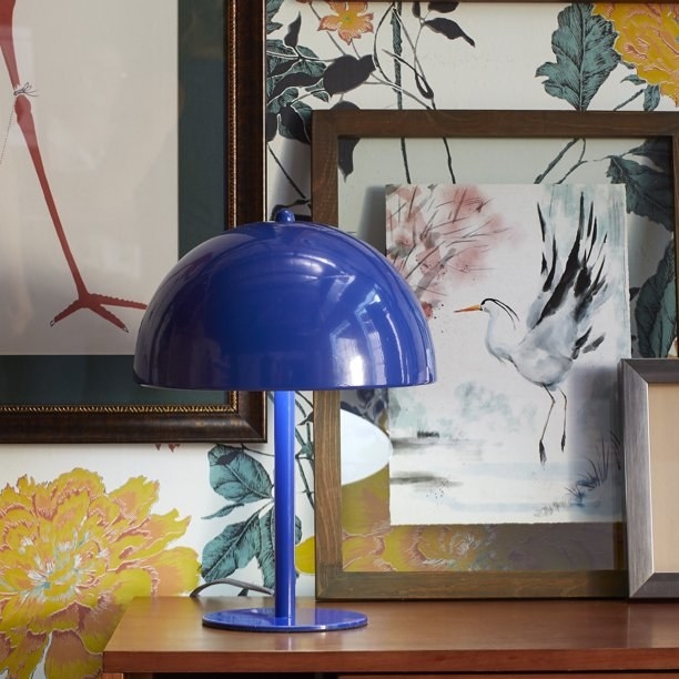 The lamp, which is royal blue and has a flat circular base, a narrow column, and a round, bowl-shaped metal shade