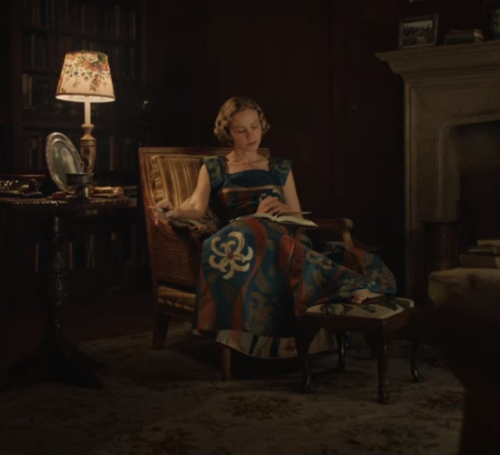 Still from The Dig: Mrs. Pretty in a colorful evening gown sitting in a library 