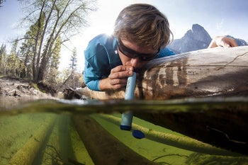 Model drinking out of blue tube directly from the river 