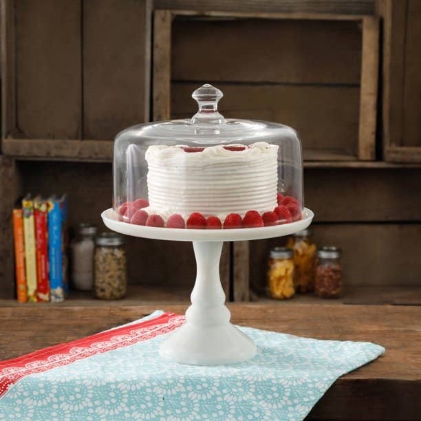 white cake stand with glass cover on a table, cake inside