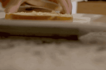 An animated GIF of a person buttering a bagel on top of a white plate.