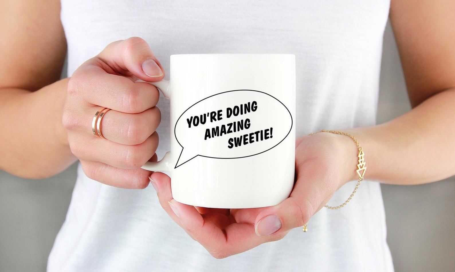 a person holding the white mug that has a thought bubble with black text inside that reads "you're doing amazing sweetie"