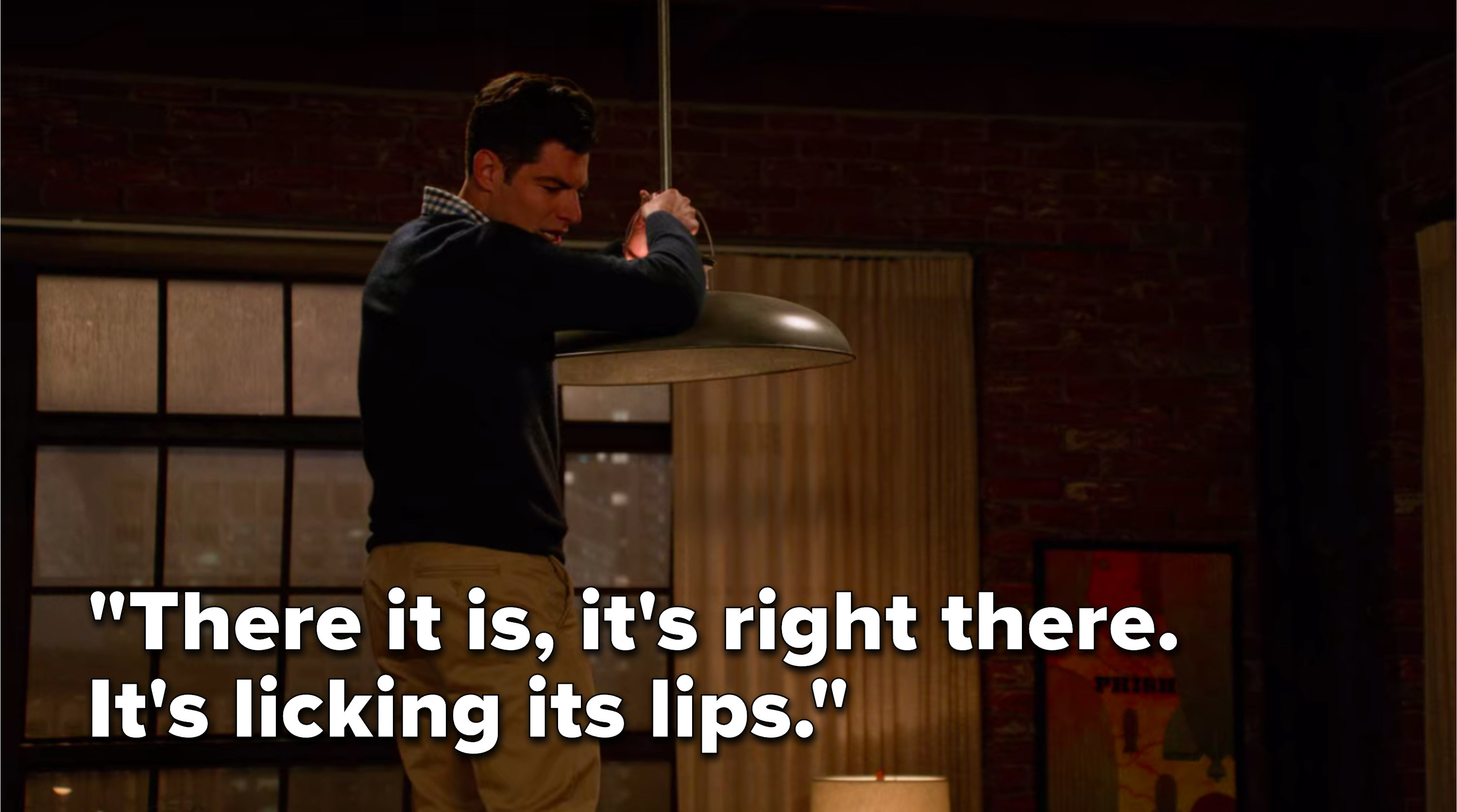Schmidt is standing on a table holding the light fixture and says, There it is, it&#x27;s right there, it&#x27;s licking its lips