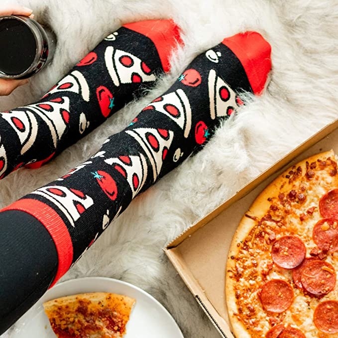 Person wearing socks with pizza print, sitting next to slide of pizza and pizza box