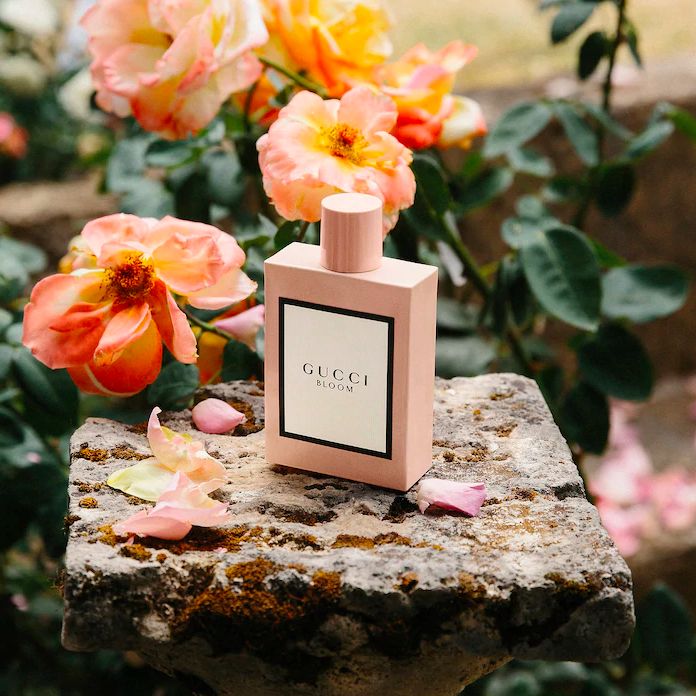 A bottle of perfume on a small rock covered in petals