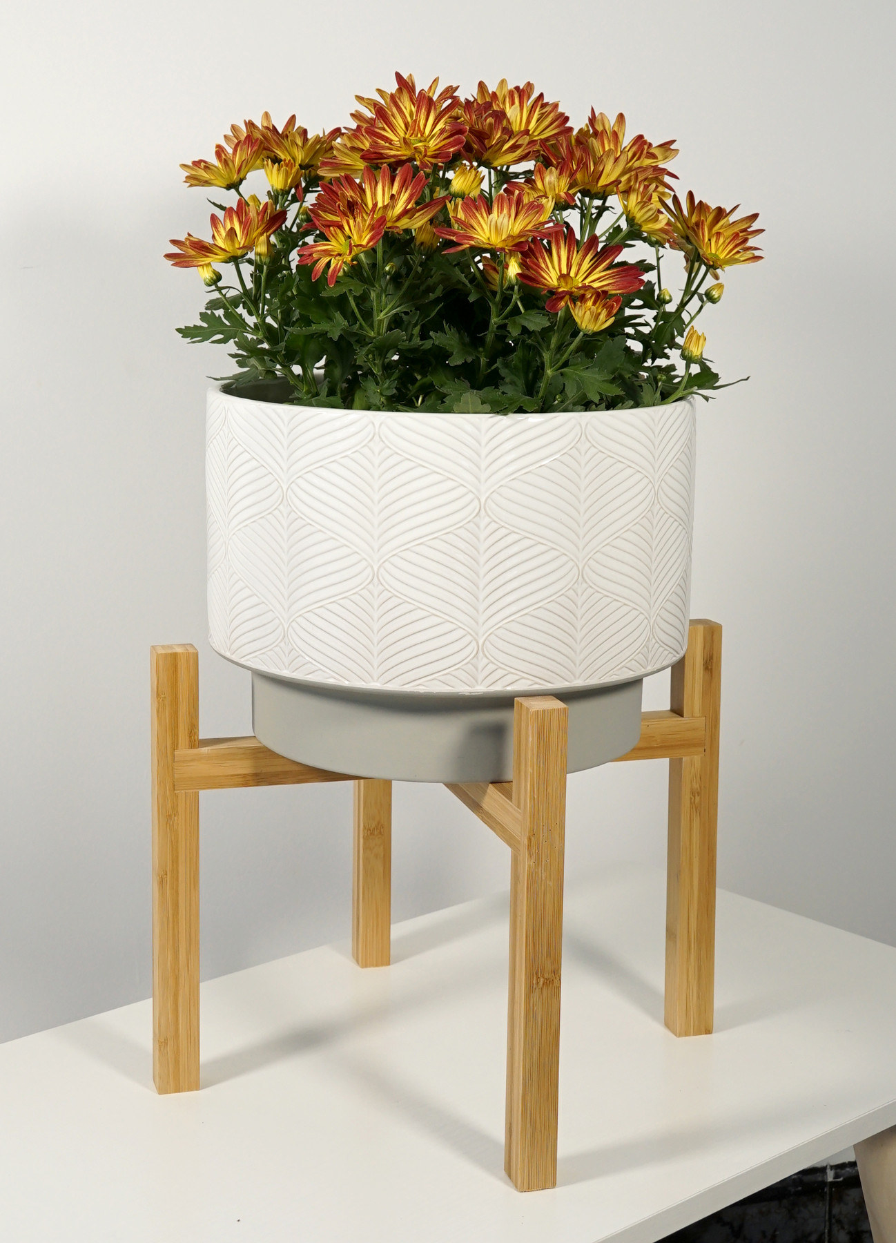 a ceramic planter with white and grey designs with a grey base on a wooden stand