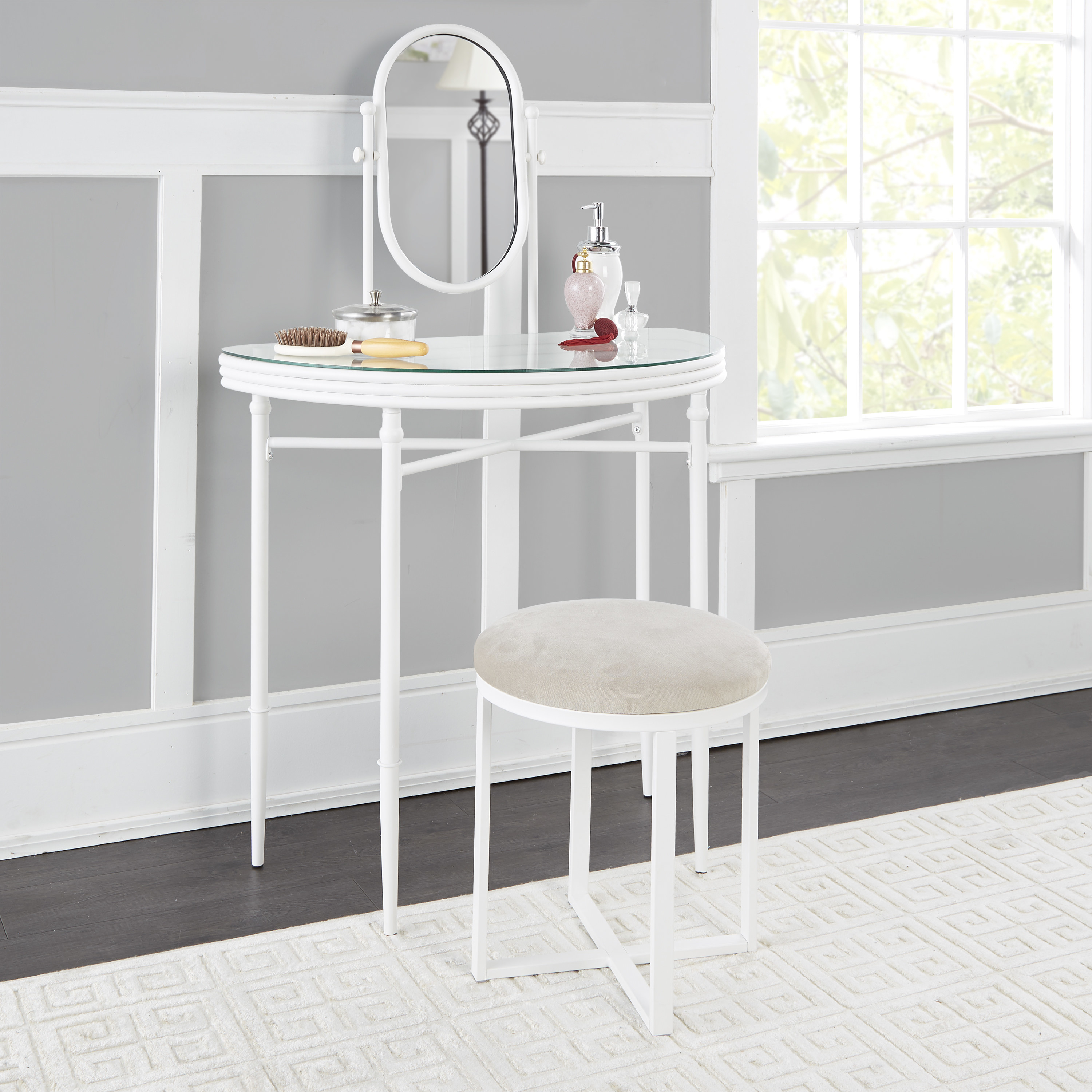 a white metal vanity with a glass top, an oval mirror, and a white metal cushioned stool