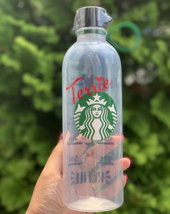 person holding clear water bottle that has starbucks logo and name printed in red on the front