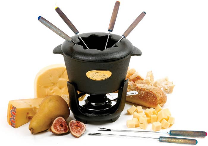 The fondue set surrounded by cheese and fruit 