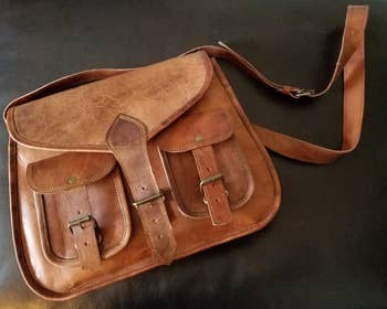 A reviewer photo of the saddle brown leather crossbody bag with a pair of front buckle pockets and a front buckle closure
