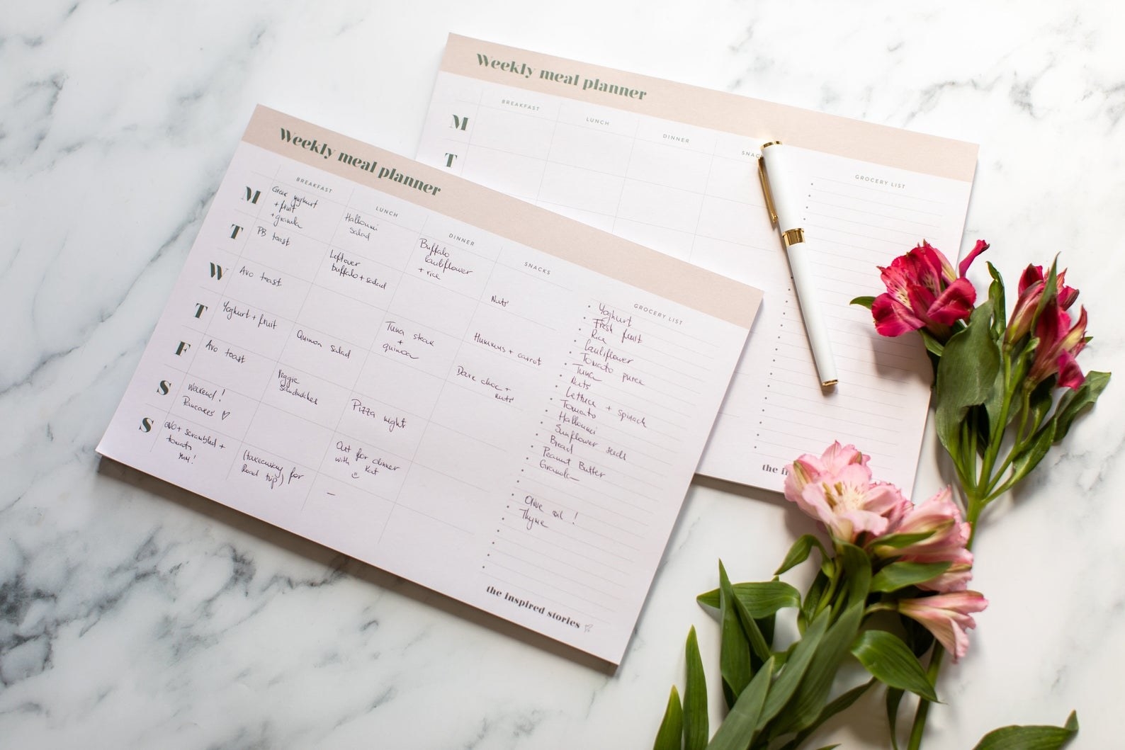 Weekly meal planner on marble table next to flowers