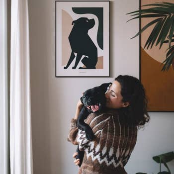 Model hugging a dog with the dog's portrait hanging on the wall behind in the 