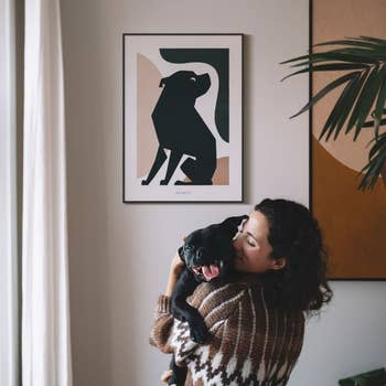 Model hugging a dog with the dog's portrait hanging on the wall behind in the 