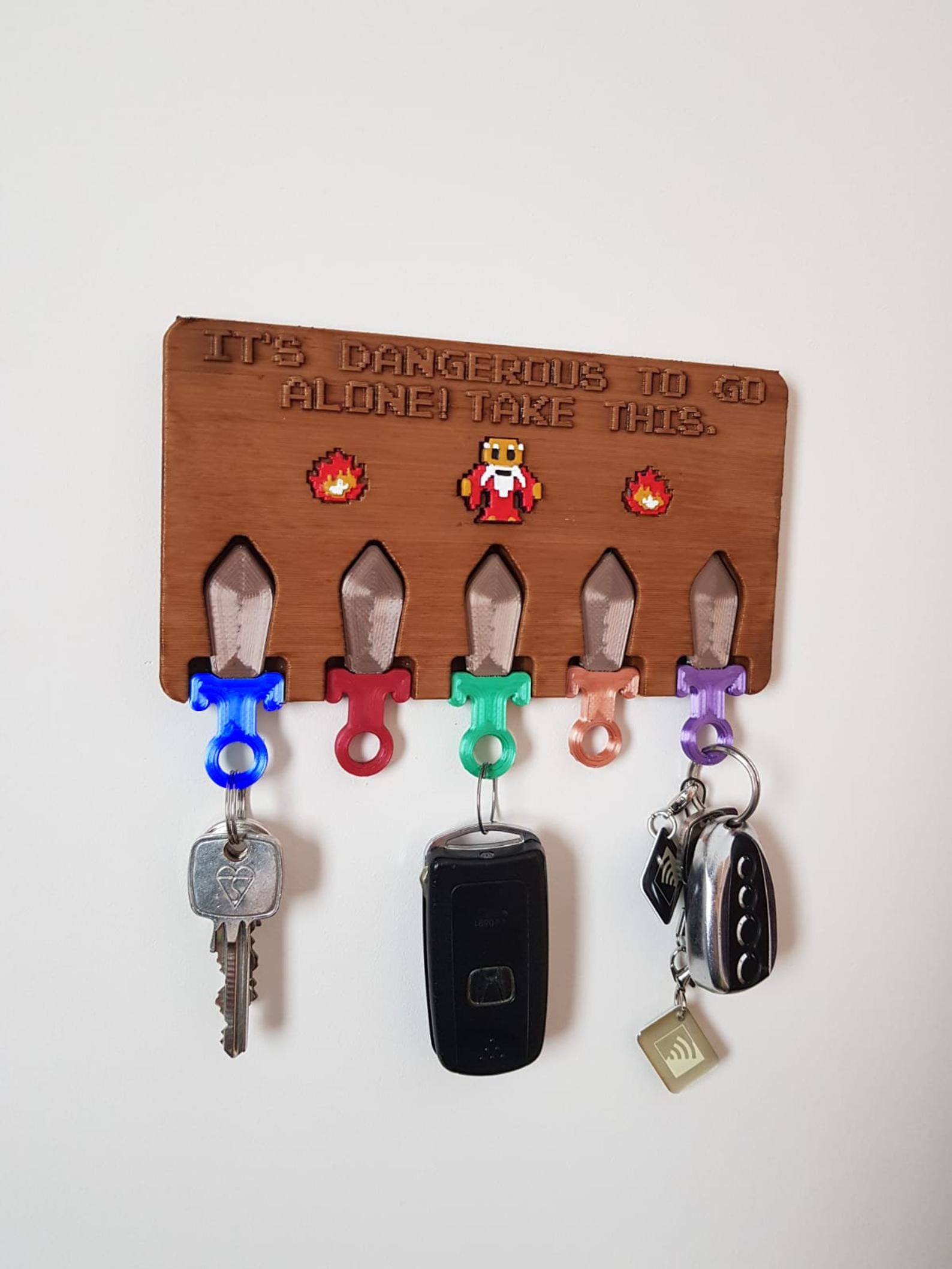 a wooden key ring holder with little swords as the hooks and the words &quot;it&#x27;s dangerous to go alone. take this&quot; above them