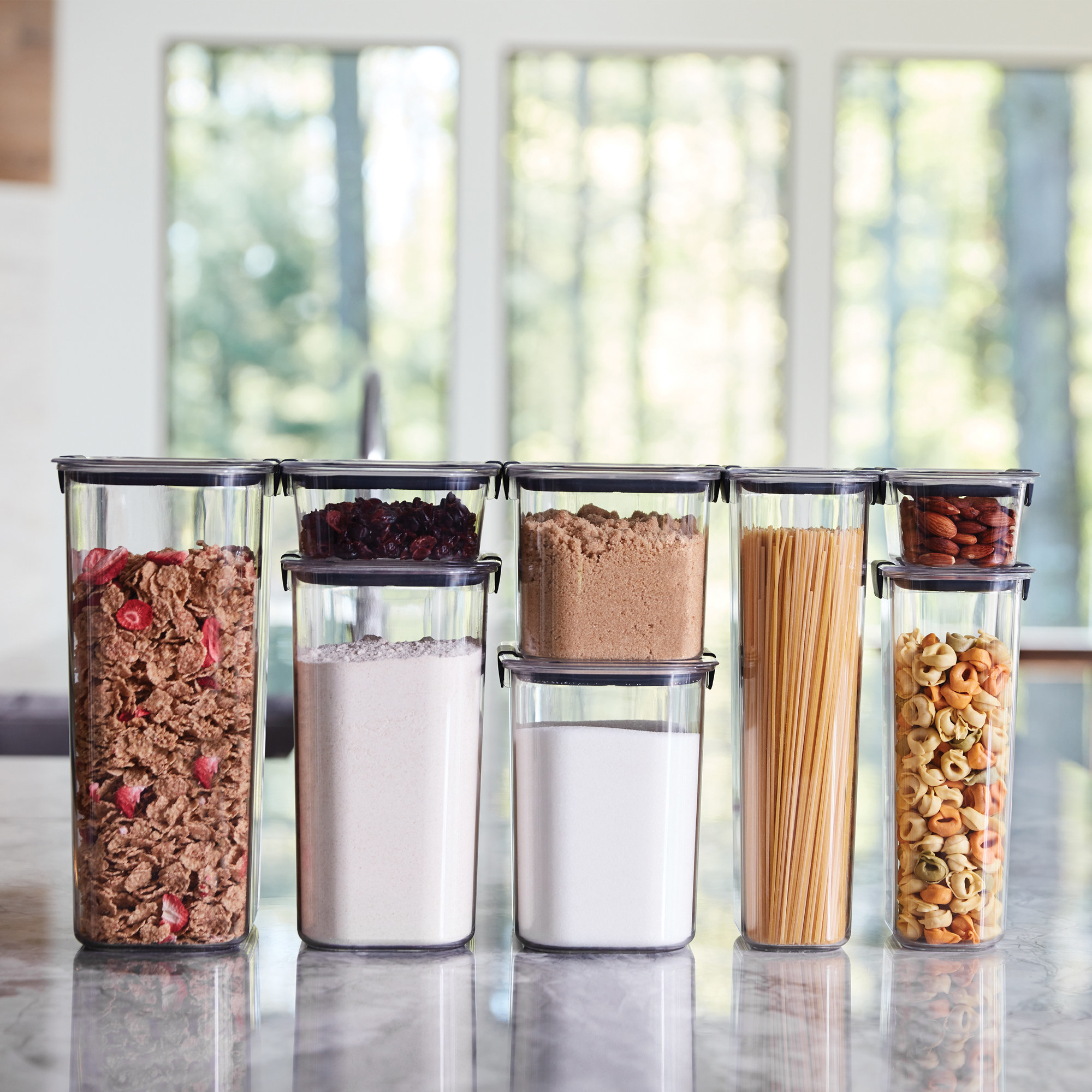 clear food storage containers filled with cereal, pasta, flour, and more, on a table
