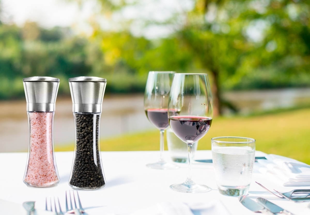 stainless steel salt and pepper shakers with glass base on a table, filled with pink salt and peppercorns