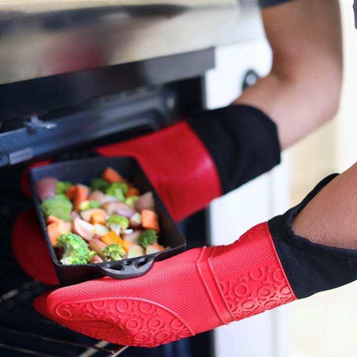 Model wearing red silicone oven mitts while taking pan out of oven