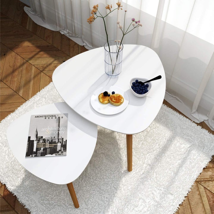 Set of two nesting tables placed in living room with food, flowers, and a magazine on top