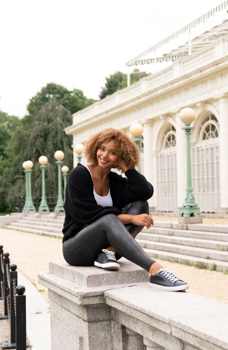 A model wearing the leggings and matching leather shoes while sitting on a railing