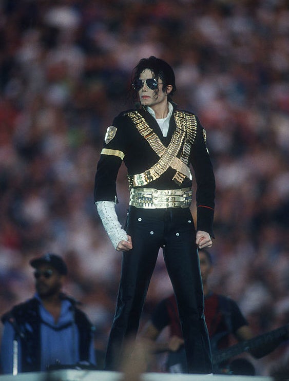 Michael Jackson posing in black suit with a gold X on the front