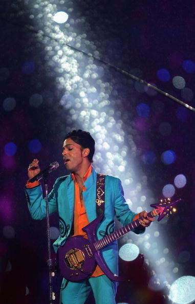 Prince singing into a microphone and holding a purple guitar